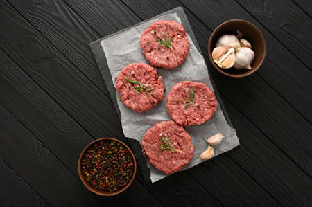 Raw beef burger patties on butcher's wooden board, rosemary and pepper. Black background. view from above.の写真素材