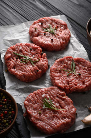 Raw beef burger patties on butcher's wooden board, rosemary and pepper. Black background. view from above.の写真素材
