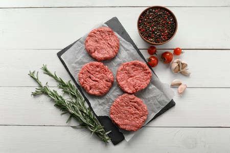 Raw beef burger patties on butcher's wooden board, rosemary and pepper. white background. view from above.の写真素材