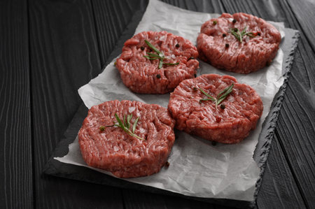 Raw beef burger patties on butcher's wooden board, rosemary and pepper. Black background. view from above.の写真素材