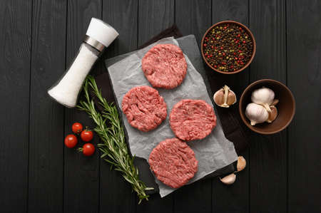 Raw beef burger patties on butcher's wooden board, rosemary and pepper. Black background. view from above.の写真素材