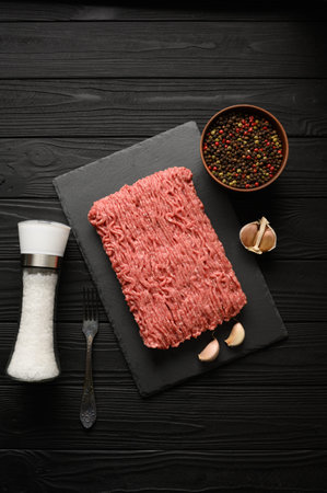 Fresh raw meat or ground chicken meat on a wooden cutting board with thyme, spices and garlic. Black...