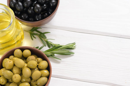 Black and green olives on a white wooden background.