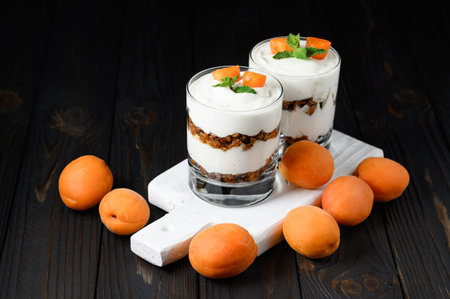 Homemade layered dessert with fresh apricot, cream cheese or yogurt, granola on rustic background.