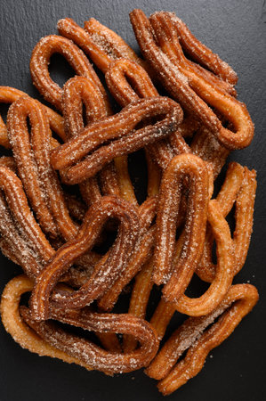 Homemade churros on a wooden black background.