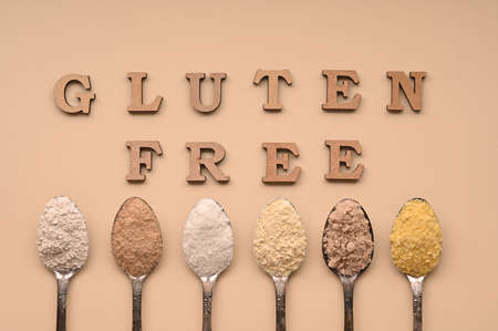 Gluten free text and spoons of various gluten free flour, almond buckwheat, rice, corn, oat, chickpea. Flat lay, top.の写真素材