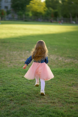 A little girl 3 years old in a summer dress runs away from the camera. The girl is turned back. summertime.の写真素材