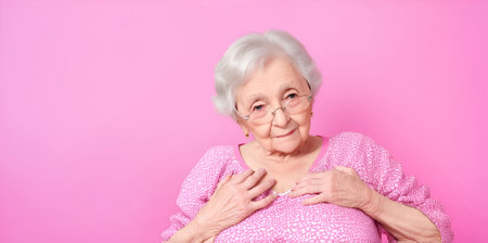 An elderly woman knows that she has breast cancer and keeps her hands on her chest on a pink background.の素材
