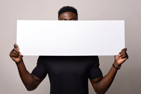 Happy young black man holding blank white banner sign, isolated studio portraitの素材