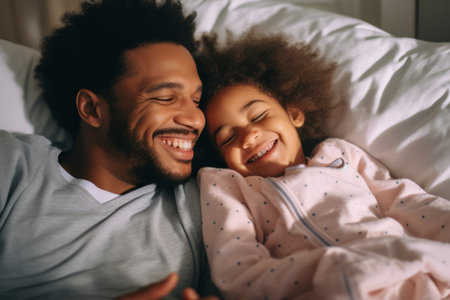 Happy loving young Black dad holding adorable mixed race baby daughter having fun in bed at home. Smiling African father playing with cute funny infant child girl waking up in bedroom in the morningの素材