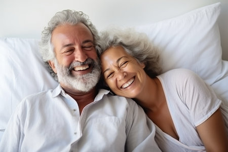 Happy senior biracial couple lying in bed and embracing at homeの素材