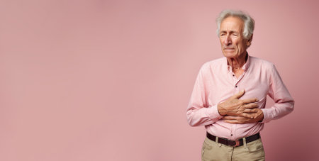 Old man holding stomach with discomfort from gastritis on pink backgroundの素材