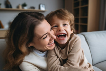 Happy young mother and little son having fun on cozy couch in living roomの素材