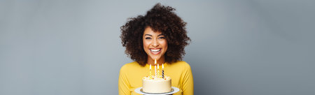 Happy African American woman with birthday cake and party hat on gray backgroundの素材