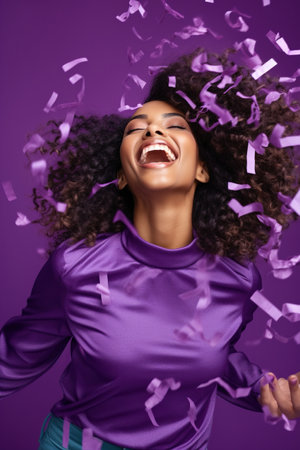 Energetic active African American lady dancing moving on holiday with flying confetti isolated on violet color backgroundの素材