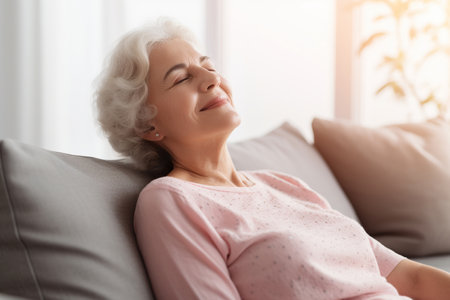 Positive tranquil elderly woman relaxing on couch with closed eyesの素材