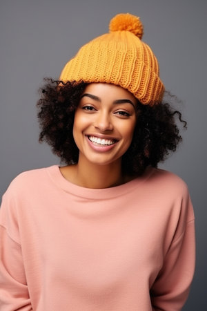 Smiling beautiful young African American woman wearing knit hat and posing cheerfully on color backgroundの素材