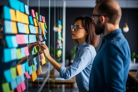 Creative people, thinking and meeting for schedule planning, brainstorming or team strategy at the office. Man and woman in teamwork decision for project plan, tasks or sticky note ideas in startupの素材