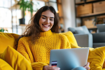 Latin Woman wearing yellow sweater sitting on yellow sofa at home and shopping online with credit cardの素材