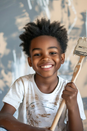 Happy young African American boy confidently holding a painting brush during home renovationの素材
