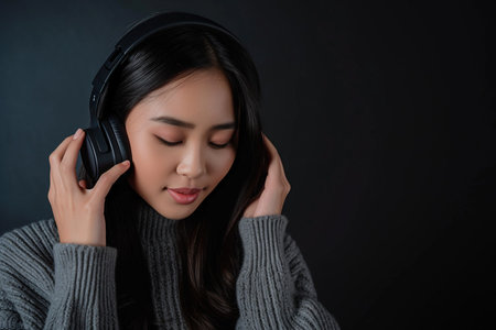 Young Asian woman wearing headphones on a black background listening to her favorite music.の素材