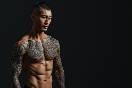 Confident Japanese man with muscular body tattooed on black background.の素材