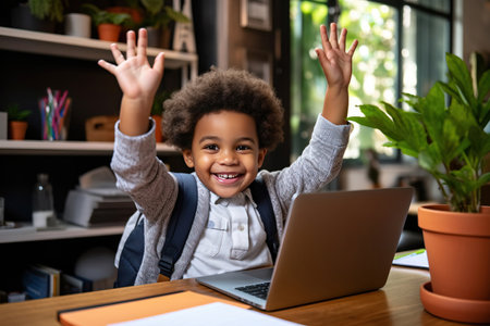 Little african american school boy raising hands up with excitement during home distance education.の素材