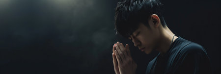 Asian man prays to god on dark studio background. Cinematic effectの素材