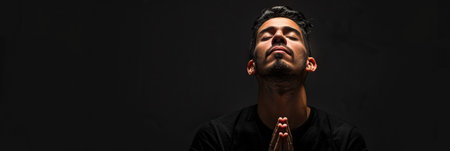 Latin American man prays to god on black studio backgroundの素材