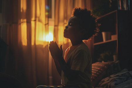 African American boy prays to god in dark children room. Cinematic effectの素材