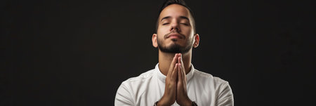 Latin American man prays to god on black studio backgroundの素材