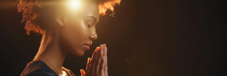 African American woman prays to god on dark studio background. Cinematic effectの素材