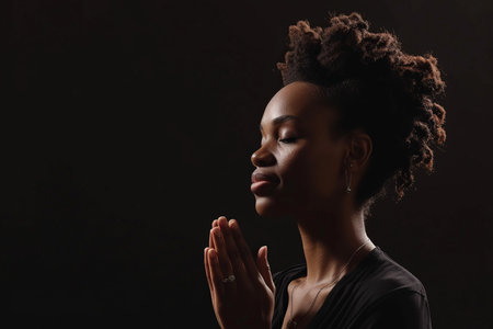 African American woman prays to god on black studio backgroundの素材