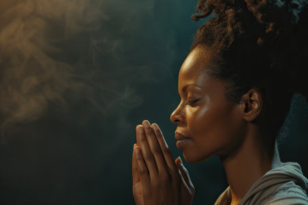 African American woman prays to god on dark studio background. Cinematic effectの素材