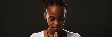 African American woman prays to god on black studio backgroundの素材