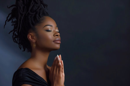 African American woman prays to god on black studio backgroundの素材