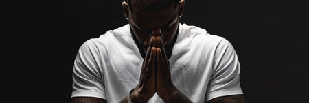 African American Man prays to god on black studio backgroundの素材
