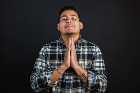 Latin American man prays to god on black studio backgroundの素材