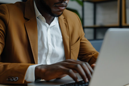 Focused African American business man typing at laptop in office closeup. Guy surfing internetの素材