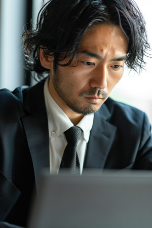 Focused Japanese business man typing at laptop in office closeup. Guy surfing internetの素材