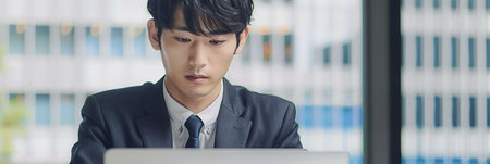 Focused Japanese business man typing at laptop in office closeup. Guy surfing internetの素材