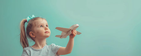 Little cute girl playing with a cardboard airplane. White retro style cardboard airplane on mint green background. Childhood dream imagination conceptの素材