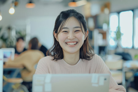 A cheerful Japanese woman expresses success and positivity while working on a laptop in a brightly lit office.の素材