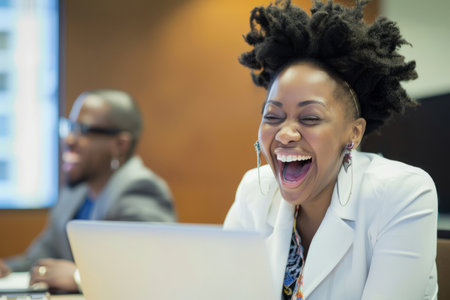 An exuberant female executive beams with happiness in the office boardroom, her laptop by her side.の素材