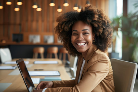 A joyful businesswoman smiles brightly in the boardroom of an office, accompanied by her laptop.の素材