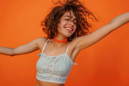 A vivacious Spanish woman dances with joyous moves to music against a bright orange backdrop.の素材
