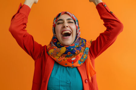 A jubilant Arab woman celebrates with vibrant moves to music against a cheerful orange background.の素材