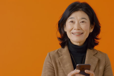 With a friendly smile, a Japanese woman, in her mid-40s, recommends a smartphone app on a vibrant orange background, blending professionalism with approachability.の素材