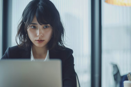 Focused young Japanese businesswoman engrossed in her laptop work in the office, displaying her proficiency and dedication to her responsibilities, amidst a sleek and minimalist office environment.の素材