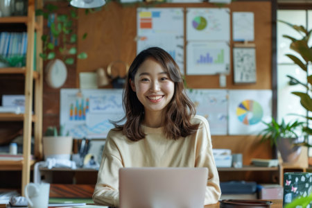 A determined Japanese startup leader girl stands at her home workplace table, surrounded by marketing financial reports and a laptop computer. With a toothy smile, she poses for the camera, emanating ambition and resolve in her entrepreneurial efforts.の素材